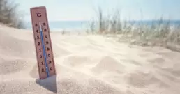 Un termometro per misurare la temperatura infilato nella sabbia con vista mare