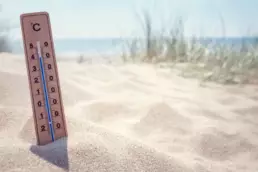 Un termometro per misurare la temperatura infilato nella sabbia con vista mare